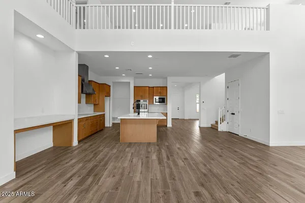 a view of an empty room and kitchen with wooden floor