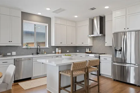 a kitchen with a refrigerator a stove a sink and white cabinets with wooden floor