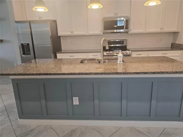 a kitchen with stainless steel appliances granite countertop a sink a microwave a refrigerator and a counter top