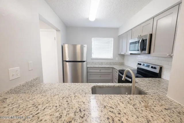 a kitchen with stainless steel appliances granite countertop a refrigerator a stove a microwave oven with white cabinets and wooden floor