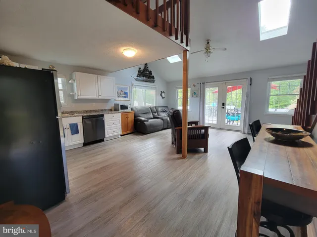 a living room with stainless steel appliances furniture a kitchen view dining table wooden floor and a window