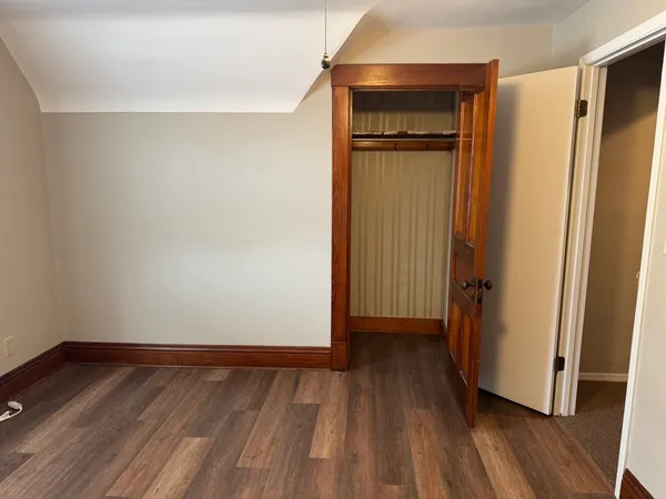 a view of an empty room with wooden floor and closet area