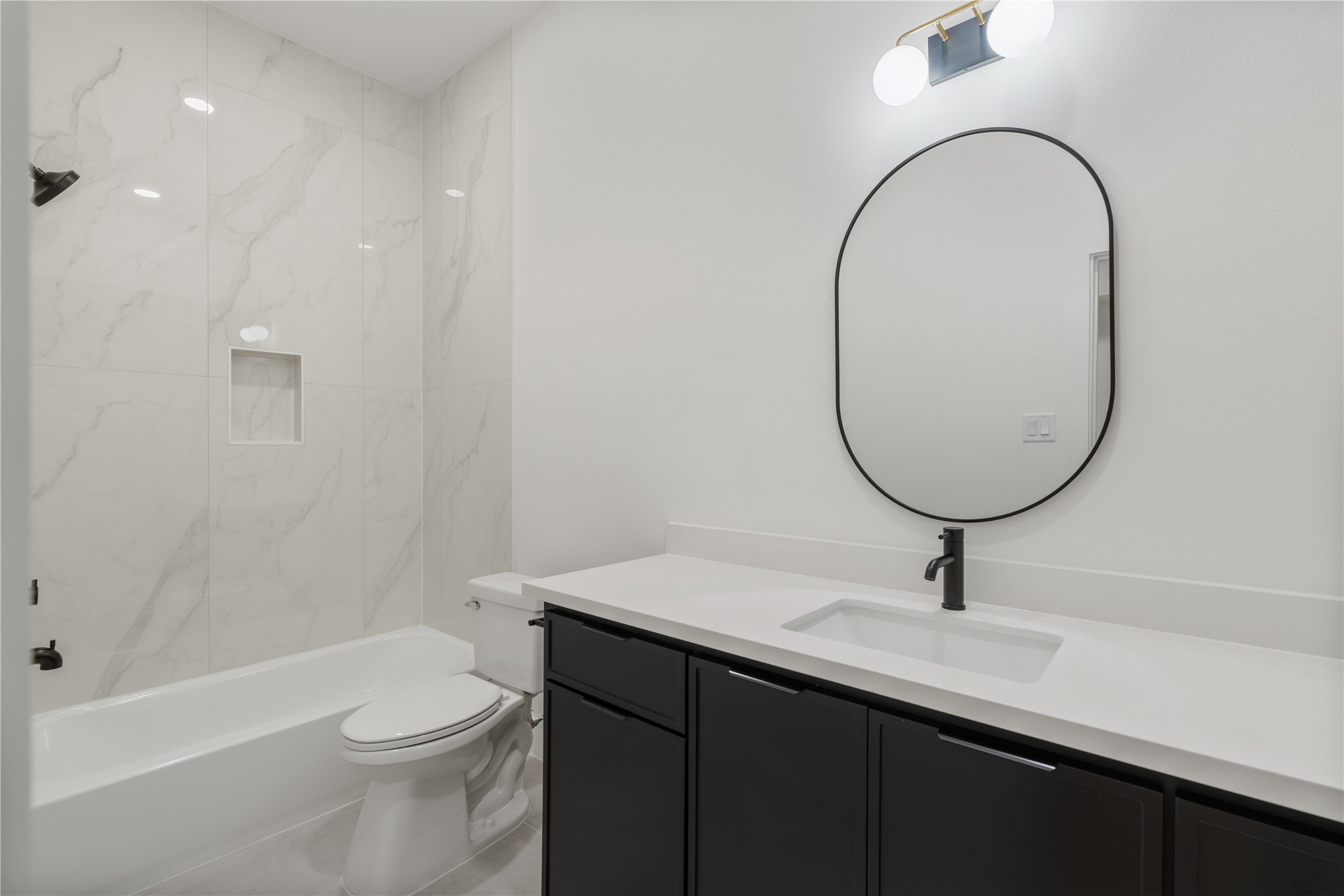 7319 Laura Koppe Road Houston, TX 77028 - Photo 33 of 42 Elegant bathroom featuring a sleek black vanity, modern fixtures, and a stylish oval mirror, complemented by a pristine white tub and marble-patterned tiles for a contemporary feel.