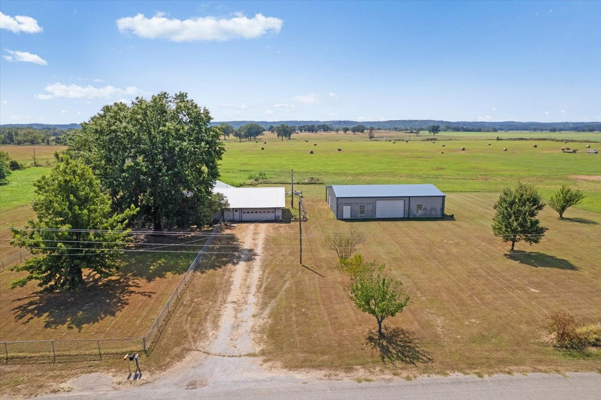 Spacious property featuring a single-story residence, detached metal outbuilding, expansive grassy grounds, mature trees, and a gravel driveway