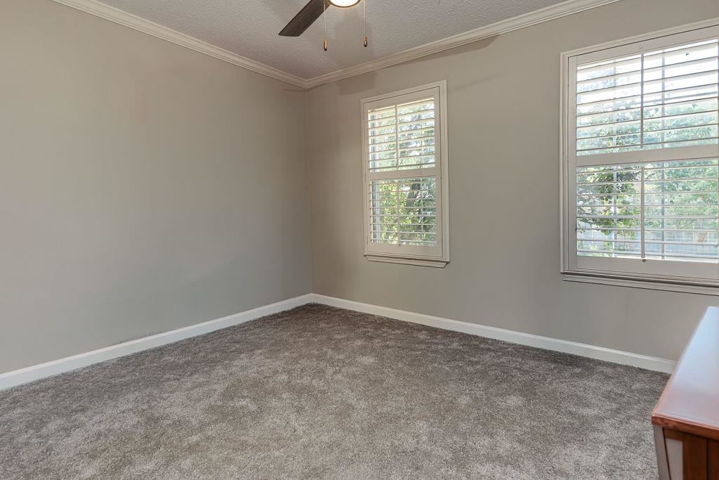 9768 Riggin Drive Memphis, TN 38002 - Photo 25 of 32 Interior room featuring two windows with white plantation shutters, gray carpet flooring, light gray wall paint, white baseboards, and crown molding