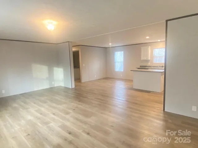 a view of empty room with wooden floor and kitchen