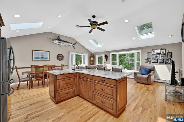 a open kitchen with stainless steel appliances granite countertop a refrigerator a stove dining table and chairs with wooden floor