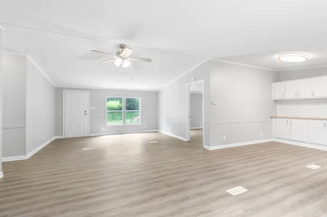 an empty room with wooden floor chandelier fan and windows