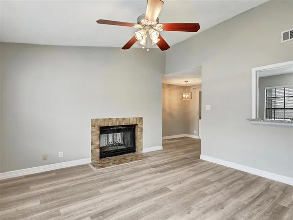 a view of an empty room with wooden floor fireplace and a window