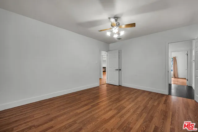 a view of an empty room with wooden floor and a ceiling fan