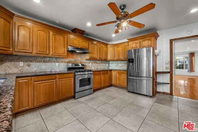 a kitchen with granite countertop a refrigerator a sink a stove top oven and cabinets