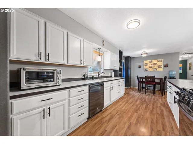 a kitchen with stainless steel appliances granite countertop a refrigerator a stove a sink dishwasher and white cabinets with wooden floor