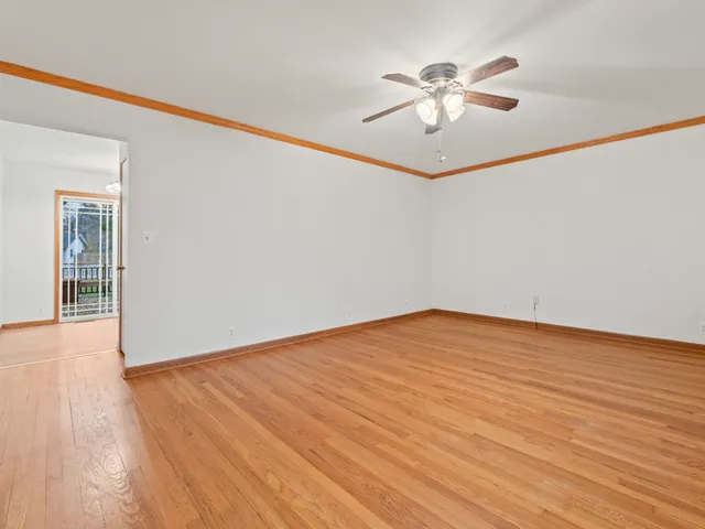 a view of an empty room with wooden floor and a ceiling fan