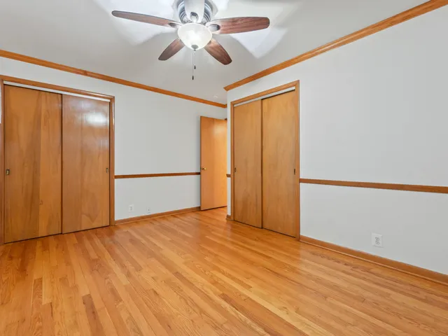 an empty room with wooden floor chandelier fan and windows