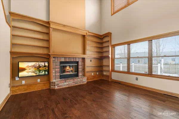a view of an empty room with wooden floor fireplace and a window