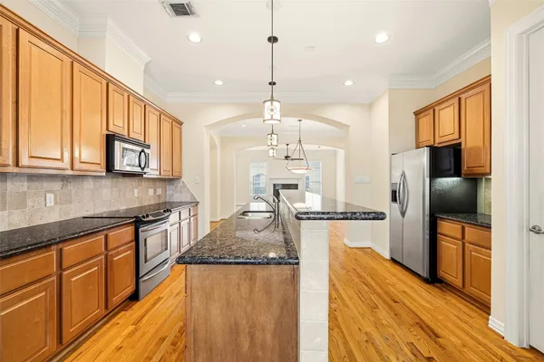 a kitchen with stainless steel appliances granite countertop a refrigerator a stove top oven a sink dishwasher and wooden cabinets with wooden floor