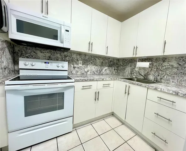 a kitchen with granite countertop white cabinets appliances and a sink