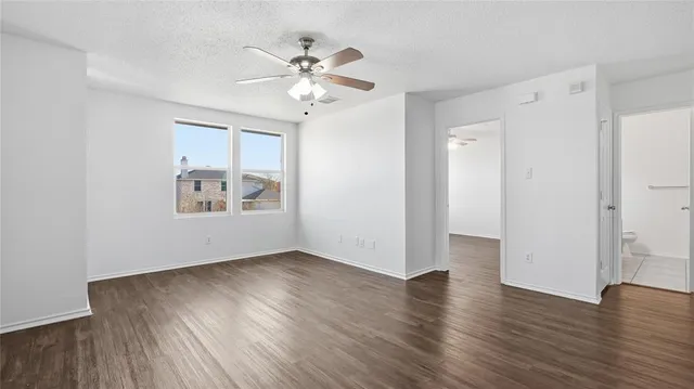 an empty room with wooden floor chandelier fan and windows