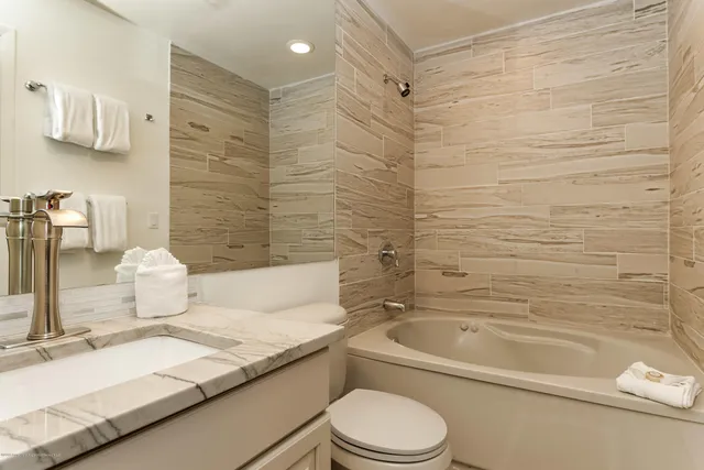 a bathroom with a granite countertop bathtub sink vanity mirror and toilet