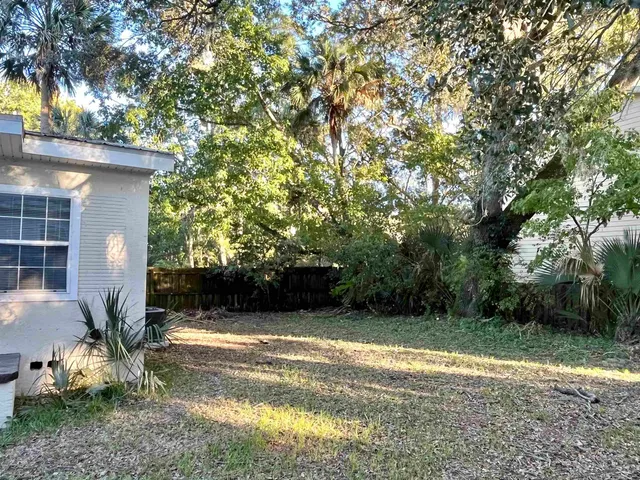 a view of yellow house with large trees and plants
