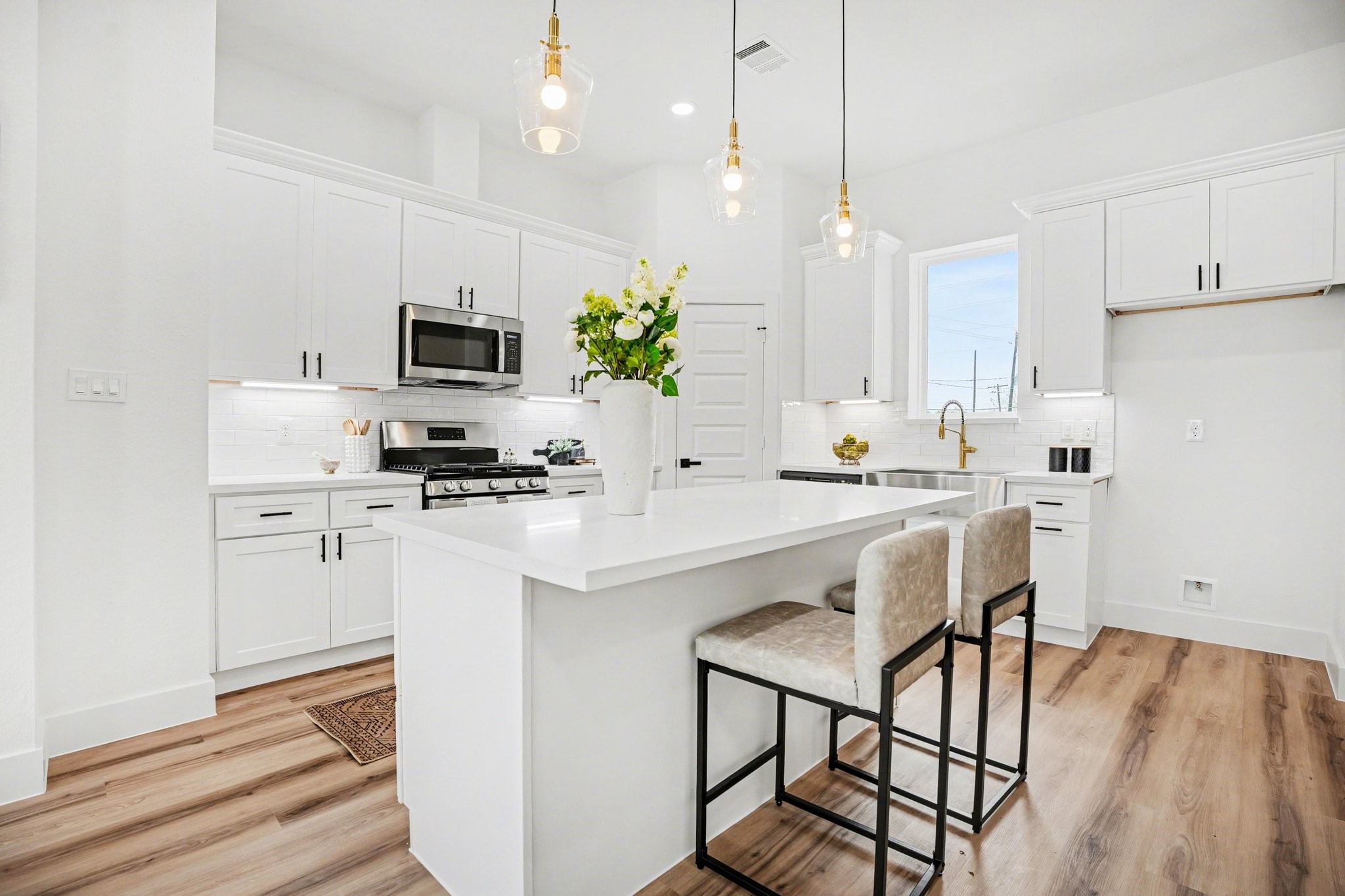 115 Milby Street Houston, TX 77003 - Photo 7 of 28 This modern kitchen features sleek white cabinetry, stainless steel appliances, and a spacious island with seating. Pendant lighting adds elegance, while wood flooring provides warmth and style.