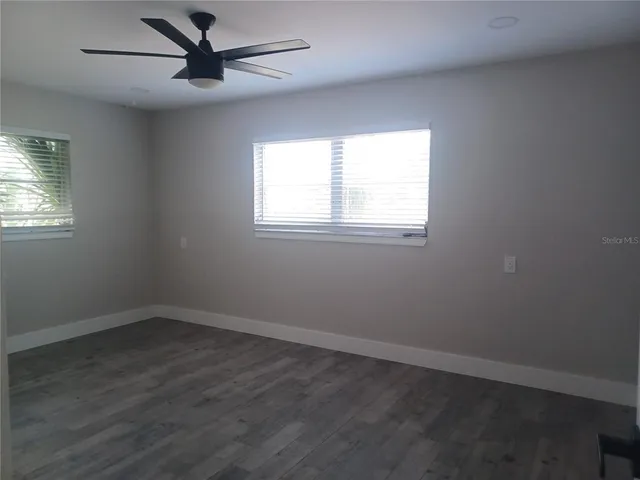 an empty room with wooden floor ceiling fan and windows