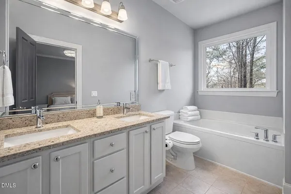 a bathroom with a granite countertop toilet a sink a mirror a window and a bathtub
