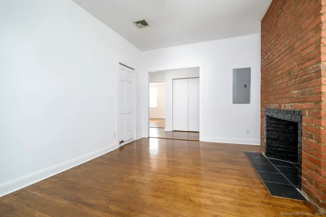 a view of an empty room with wooden floor and a fireplace