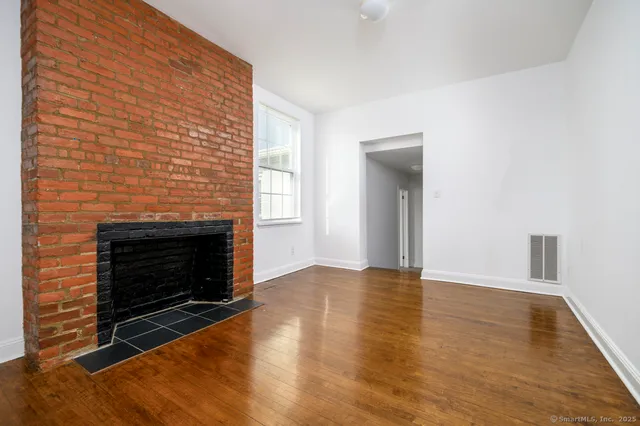 a view of an empty room with wooden floor fireplace and a window