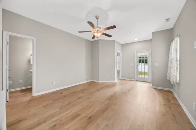 a view of an empty room with wooden floor and a ceiling fan