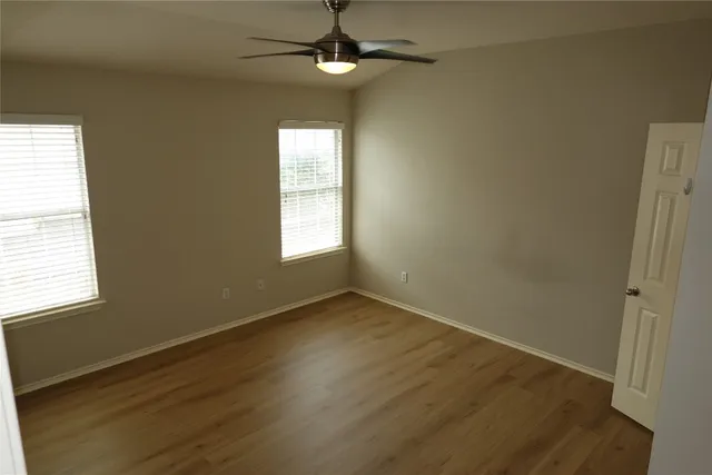 an empty room with wooden floor fan and windows