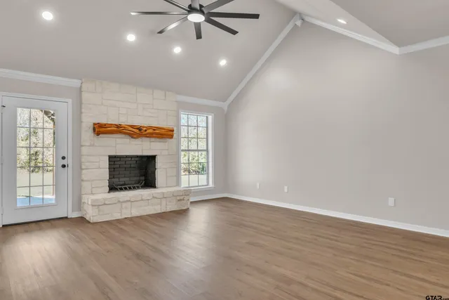 an empty room with wooden floor fireplace and windows