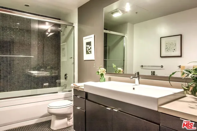a bedroom with a bed and a lamp on dresser with wooden floor
