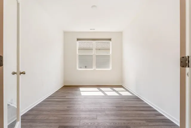 an empty room with wooden floor closet and windows