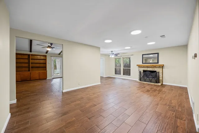 an empty room with wooden floor fireplace and windows