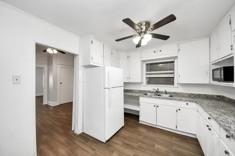 a kitchen with granite countertop a refrigerator a sink and white cabinets