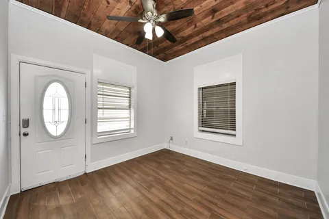 an empty room with wooden floor fan and windows