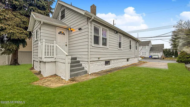 a view of a white house with a big yard plants and large tree
