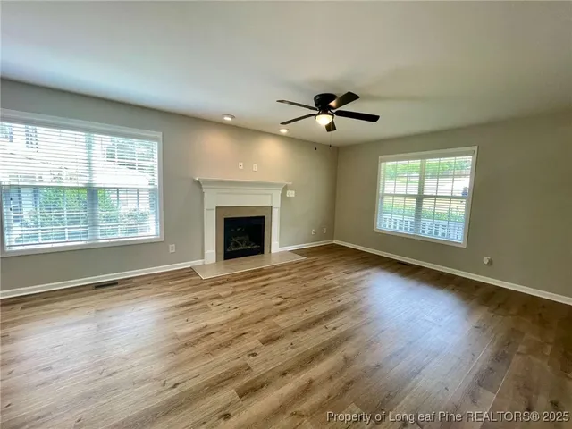 a view of an empty room with wooden floor fireplace and a window
