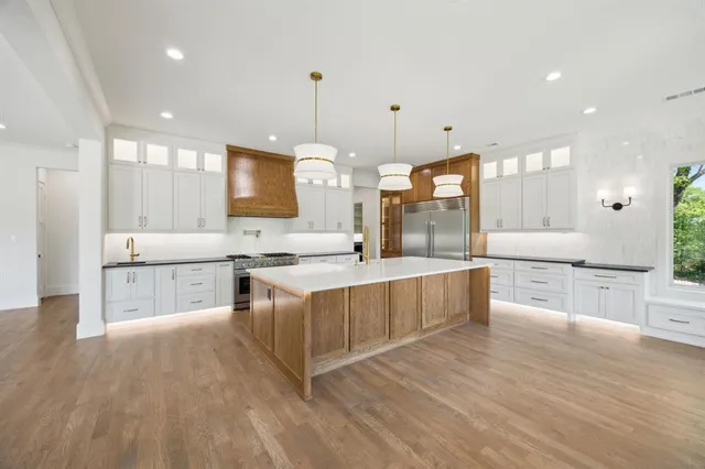 a large kitchen with stainless steel appliances a large counter top a sink a stove and a wooden floors