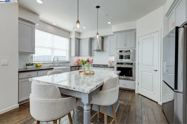 a kitchen with stainless steel appliances granite countertop a stove a sink a refrigerator white cabinets and wooden floor