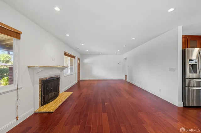 a view of an empty room with wooden floor fireplace and a window