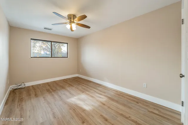 a view of an empty room with wooden floor and a ceiling fan