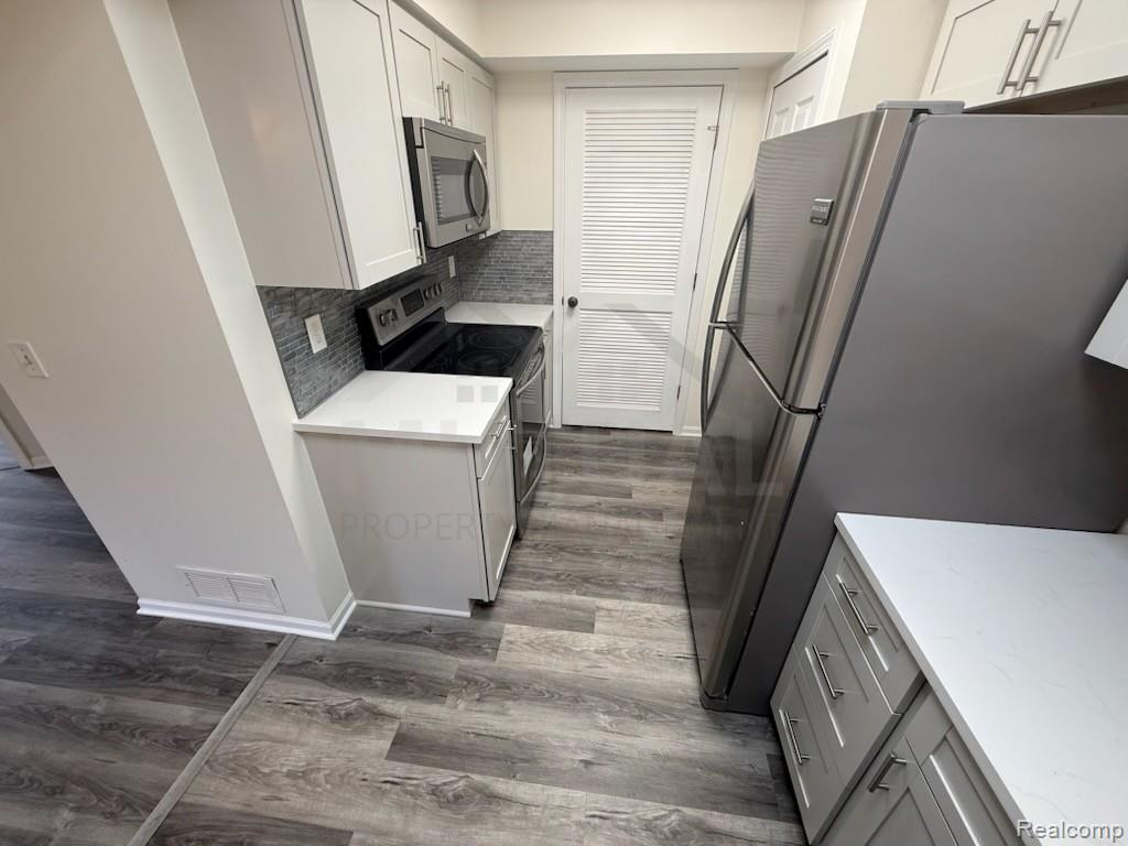 1560 Meadowside Drive Rochester, MI 48307 - Photo 7 of 17 Kitchen featuring white shaker-style cabinetry, stainless steel appliances, a tile backsplash, light-toned countertops, and wood-finish flooring