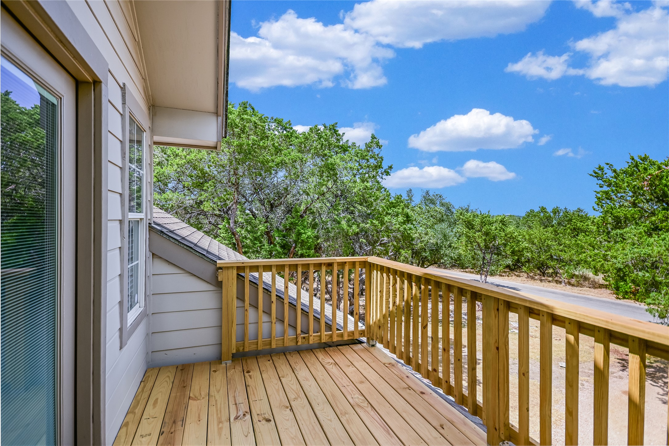 104 Crazy Cross Road Wimberley, TX 78676 - Photo 16 of 20 A wooden balcony offers sweeping views of the surrounding treetops and blue sky.