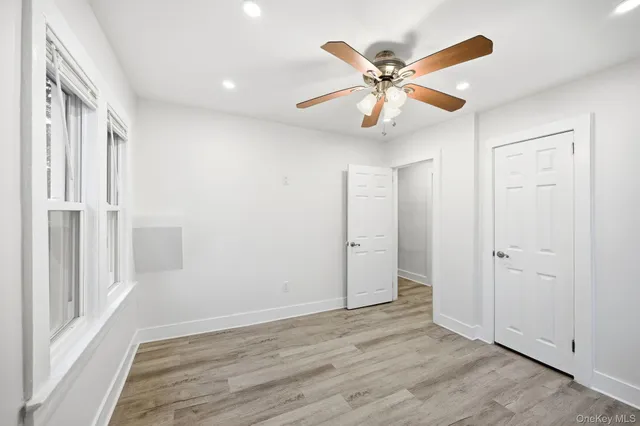 a view of an empty room with wooden floor and a ceiling fan