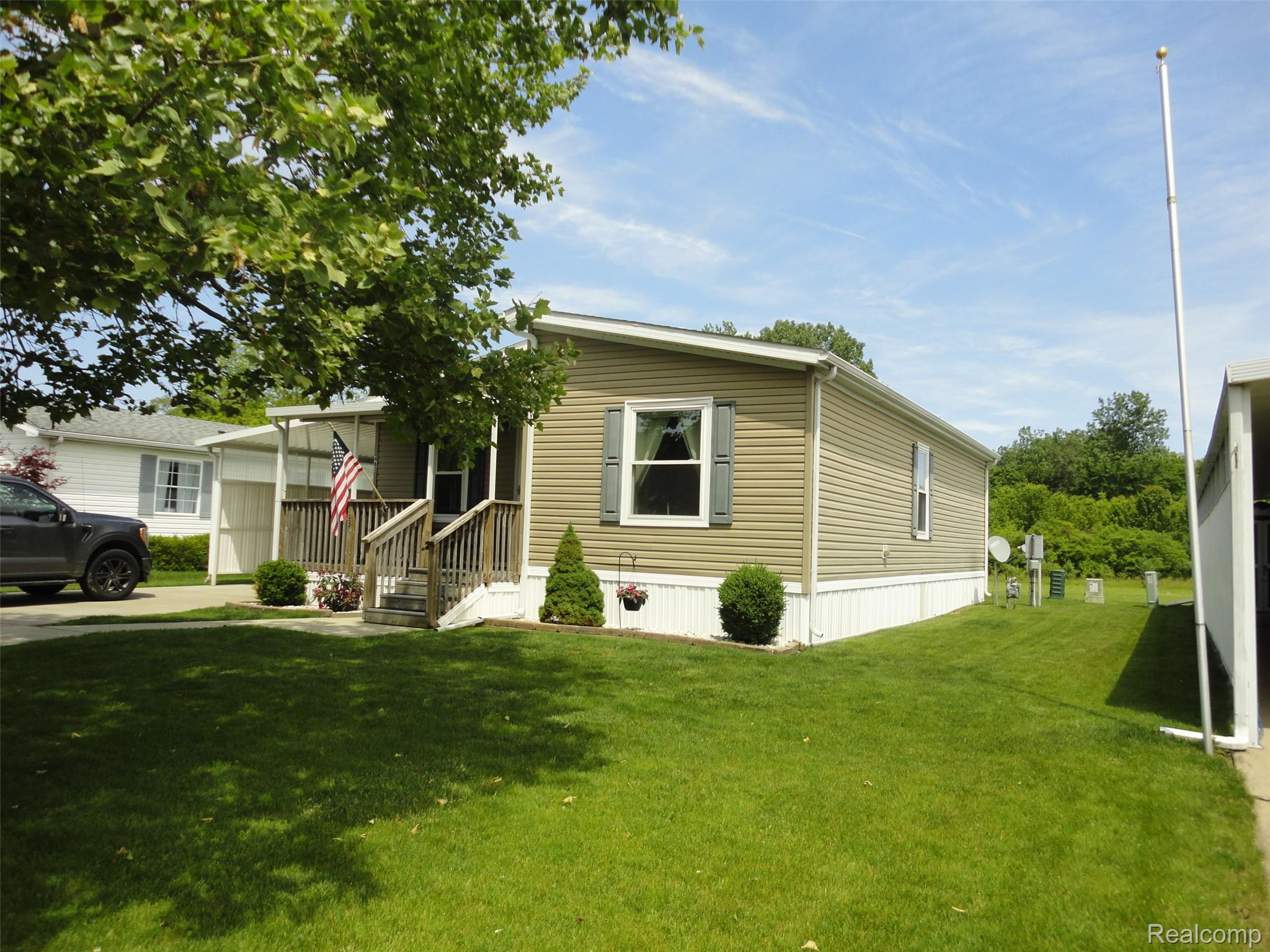 463 Edinborough Temperance, MI 48182 - Photo 14 of 23 Single-story residence featuring horizontal siding, a covered front porch with wood railings, a foundational skirting, a landscaped front yard with shrubs, and an adjacent carport structure