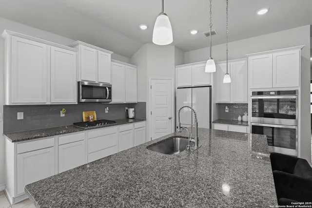 a kitchen with granite countertop a stove a sink a microwave a refrigerator and cabinets