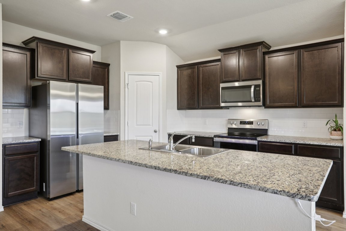 117 Break Avenue Taylor, TX 76574 - Photo 12 of 40 a kitchen with granite countertop stainless steel appliances a sink stove refrigerator and cabinets