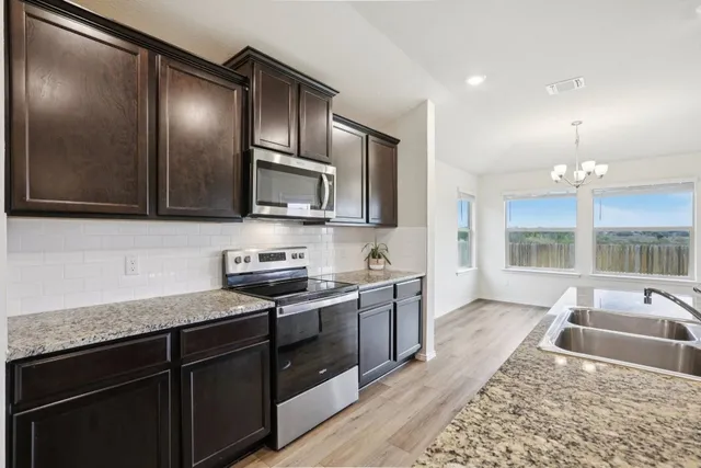 a kitchen with stainless steel appliances granite countertop a sink and stove top oven with wooden floor